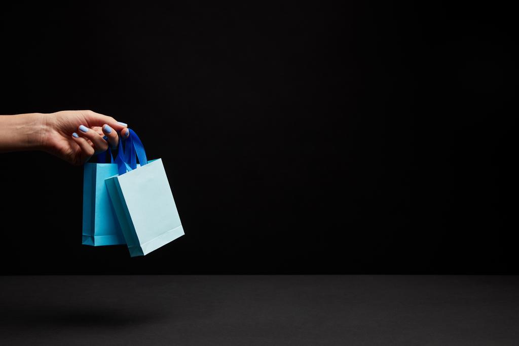 vista parcial de la mujer sosteniendo bolsas de compras de papel azul sobre fondo negro
 - Foto, imagen
