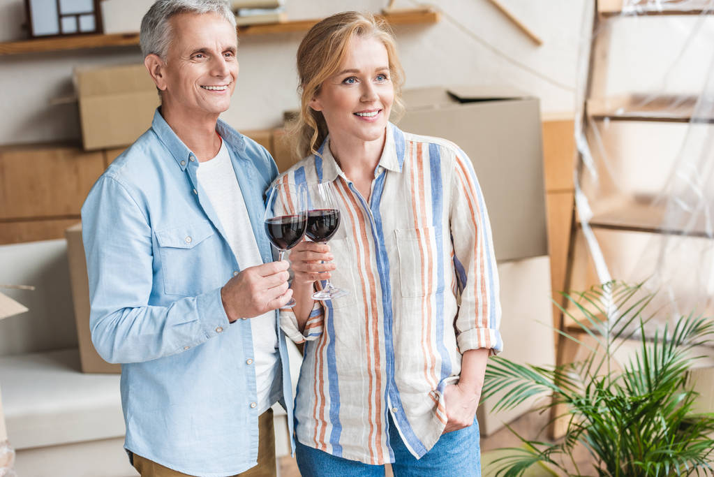 šťastný pár senior holding sklenic vína a koukal v novém domě - Fotografie, Obrázek