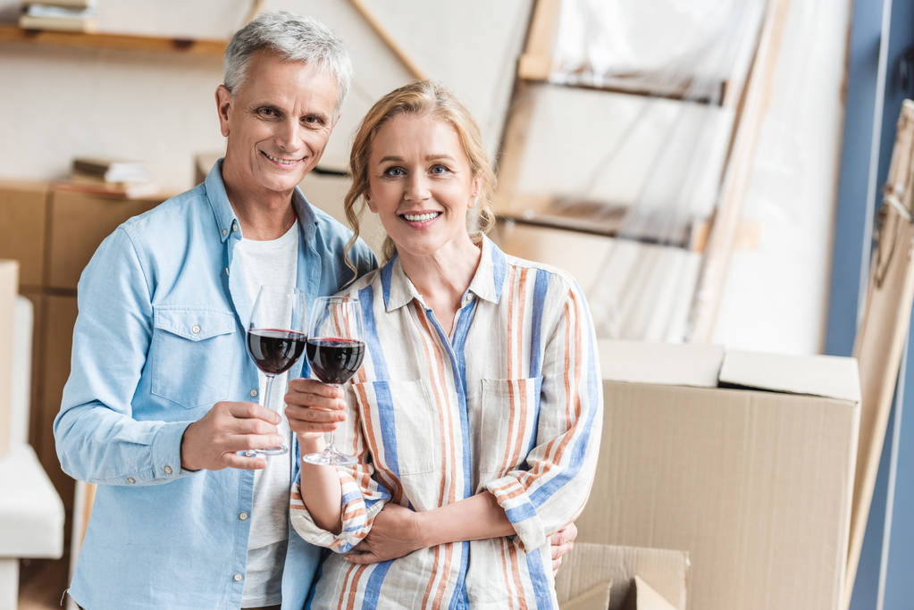 šťastný pár držení sklenice vína a usmívá se na kameru v novém bytě - Fotografie, Obrázek