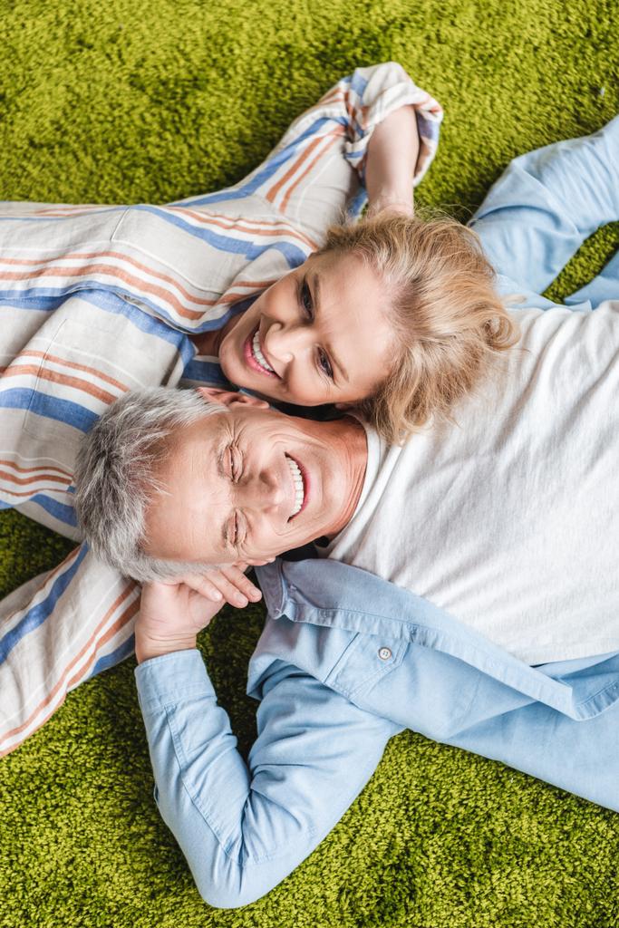 pohled shora šťastný starší pár leží vedle sebe na zelený koberec - Fotografie, Obrázek