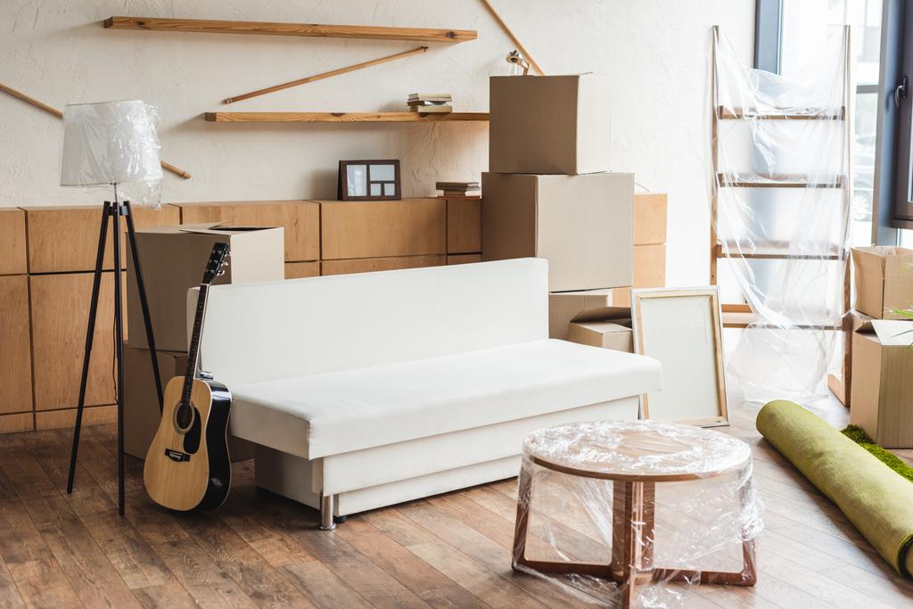 cajas de cartón, alfombra enrollada, guitarra y muebles en nuevo apartamento durante la reubicación
 - Foto, Imagen
