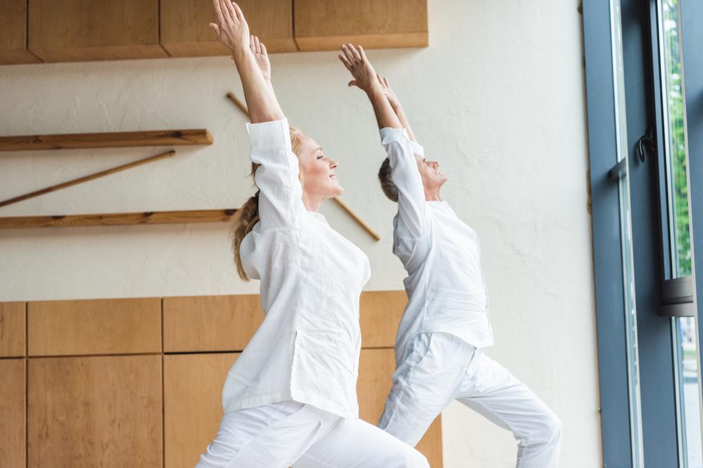 Oldalnézet, sportos felső pár teljesítő harcos póz, miközben gyakorló jóga otthon - Fotó, kép