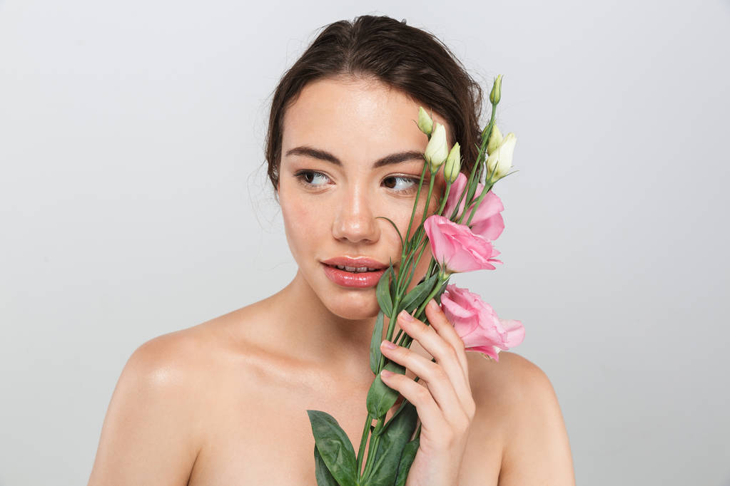 Egy csinos, fiatal félmeztelen nőt make-up jelentenek az arcát, elszigetelt, felett szürke háttér eustoma virágok szépség portréja - Fotó, kép