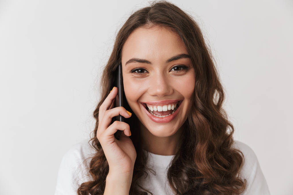 Nahaufnahme Porträt einer lachenden jungen beiläufigen brünetten Frau, die auf einem Mobiltelefon isoliert vor weißem Hintergrund spricht - Foto, Bild
