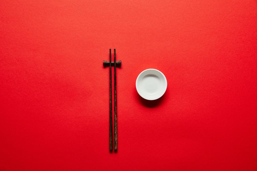 pohled shora uspořádány hůlky a prázdnou misku na červené pozadí - Fotografie, Obrázek