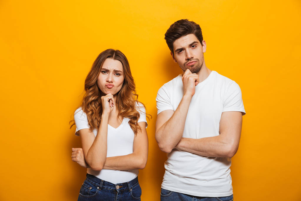 Foto von verärgerten Mann und Frau in lässiger Kleidung, die zusammen stehen und das Kinn berühren, mit irritiertem Blick isoliert vor gelbem Hintergrund - Foto, Bild
