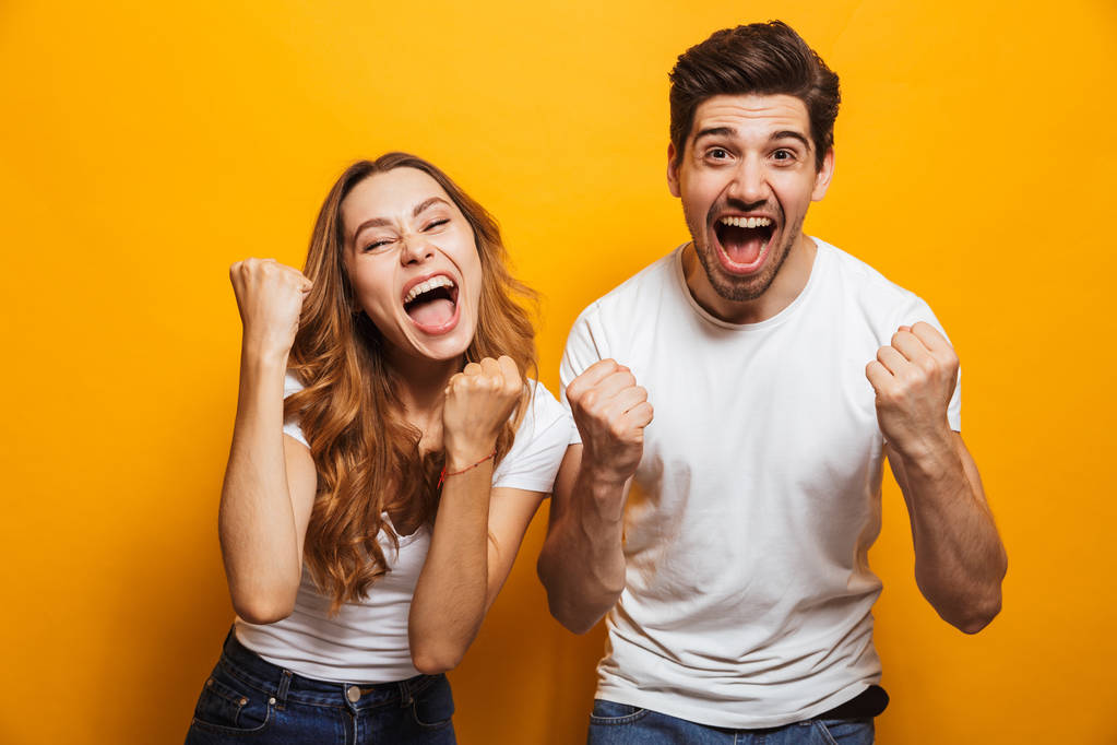 Портрет позитивного красивого мужчины и женщины в основной одежде кричат и сжимают кулаки, как победители или счастливые люди изолированы на желтом фоне
 - Фото, изображение