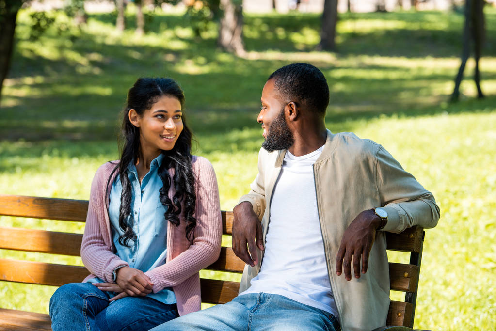 Afrikaanse Amerikaanse echtpaar zittend op houten bankje in het park en kijken naar elkaar  - Foto, afbeelding