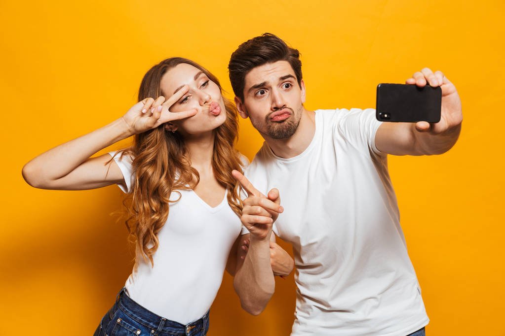 Muotokuva onnellinen mies ja nainen ottaa selfie valokuva älypuhelimeen ja näyttää rauhan merkki eristetty keltaisella taustalla
 - Valokuva, kuva