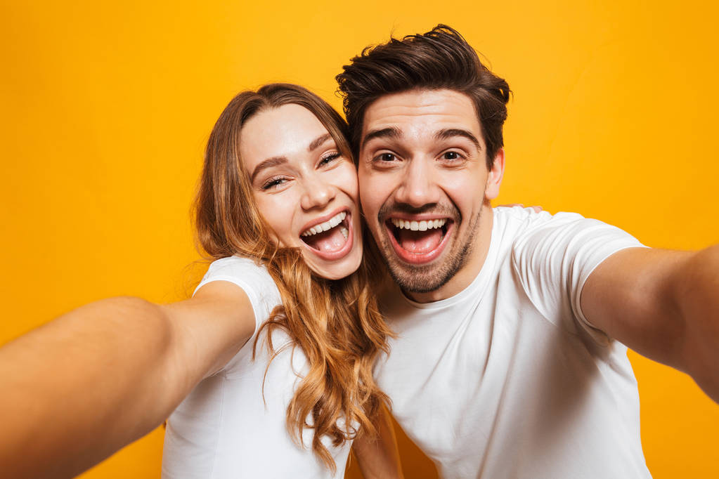 Retrato close-up de homem e mulher alegre 20s rindo e tirando foto selfie isolado sobre fundo amarelo
 - Foto, Imagem