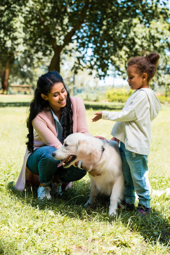 s úsměvem africké americké matka a dcera palming psa v parku - Fotografie, Obrázek