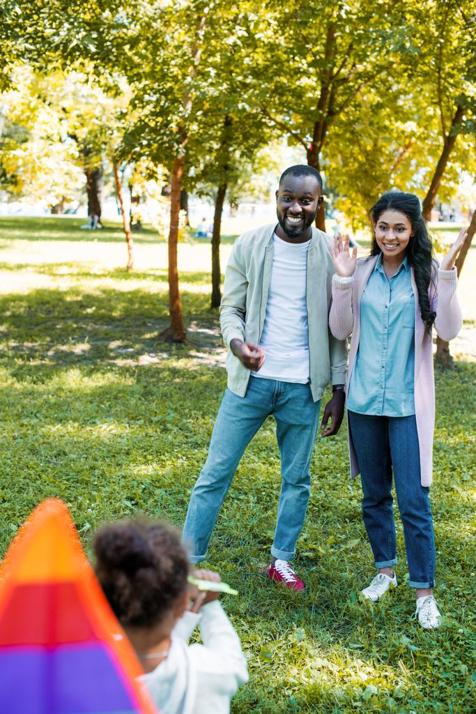 visão traseira da filha americana africana mostrando pipa para pais felizes no parque
 - Foto, Imagem