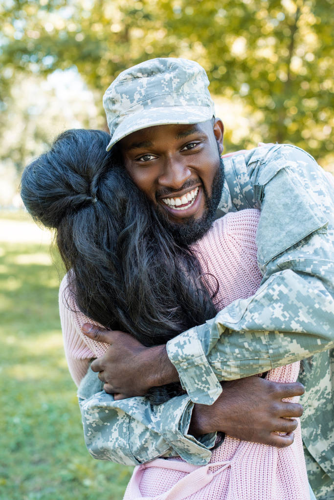 счастливый африканский американский солдат в военной форме обнимает подружку в парке
 - Фото, изображение
