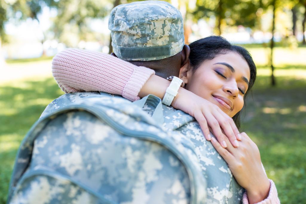 Αφρικανικός Αμερικανός στρατιώτης σε στρατιωτική στολή αγκαλιάζει ευτυχισμένη φίλη στο πάρκο - Φωτογραφία, εικόνα