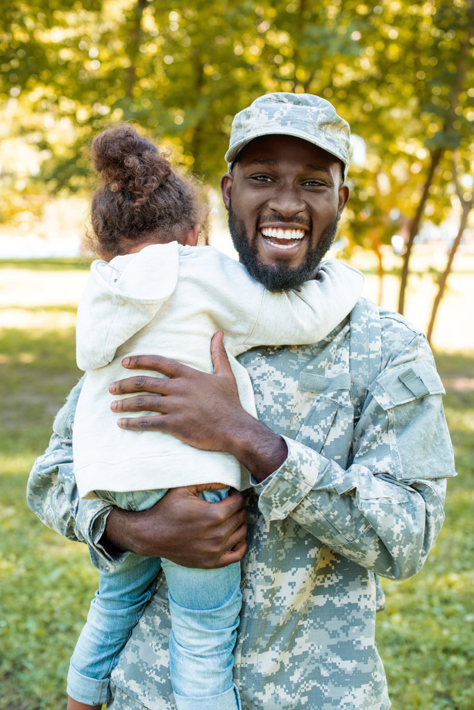 gülümseyen Afrikalı-Amerikalı asker askeri üniformalı kızı park holding - Fotoğraf, Görsel