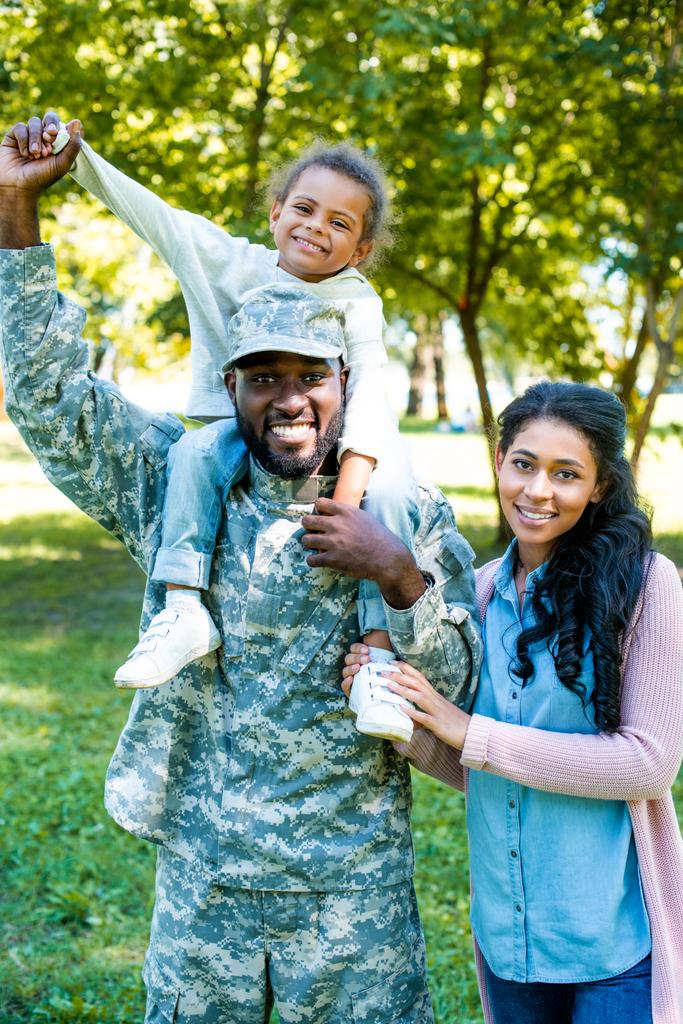 χαμογελώντας Αφρικανικός Αμερικανός στρατιώτης με στρατιωτική στολή κρατώντας κόρη στους ώμους, στο πάρκο - Φωτογραφία, εικόνα