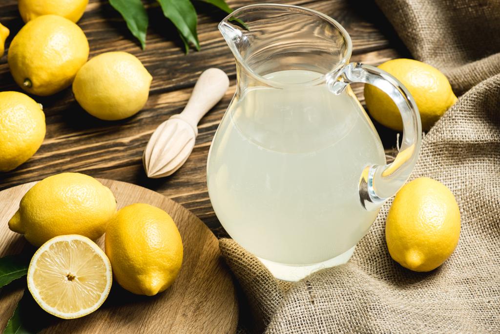 フレッシュ ジュース、絞り器、木製の表面に解任に黄色いレモンとジョッキ グラス  - 写真・画像
