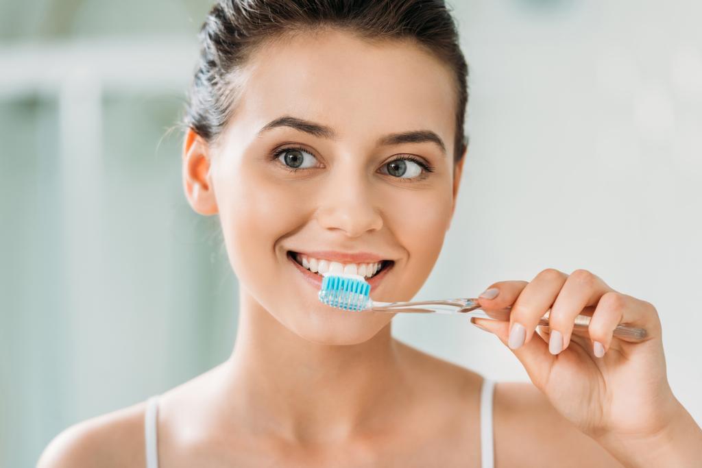 красивая улыбающаяся девушка чистит зубы в ванной комнате
 - Фото, изображение