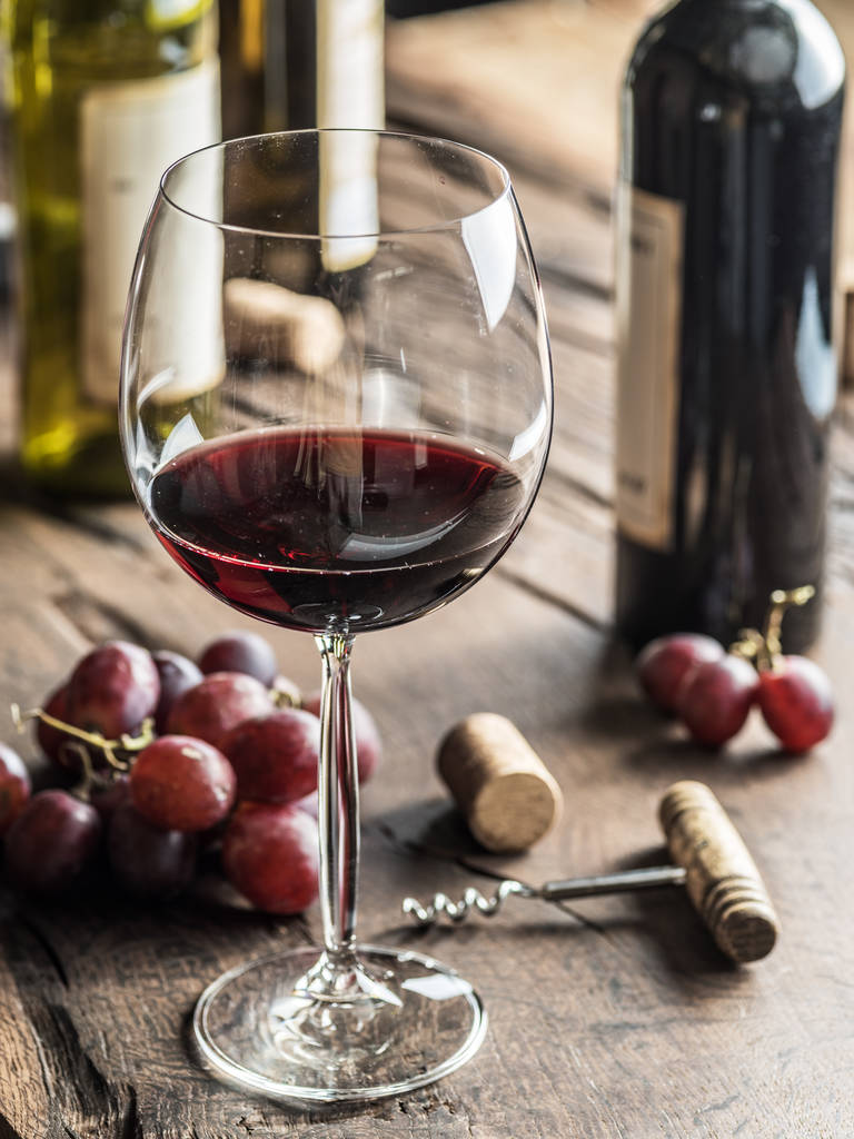 Kieliszek czerwonego wina na stole. Butelka wina i winogron w tle. - Zdjęcie, obraz