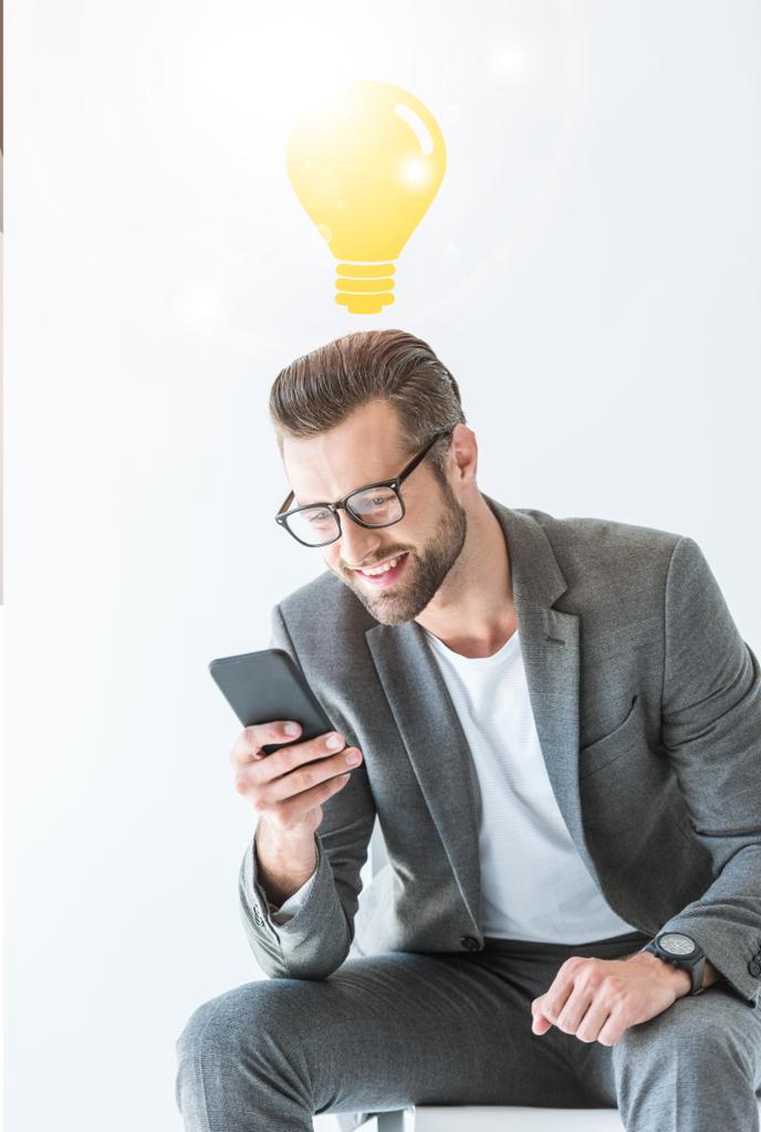 успешный бизнесмен с помощью смартфона, изолированный на белом с идеей лампочки
 - Фото, изображение