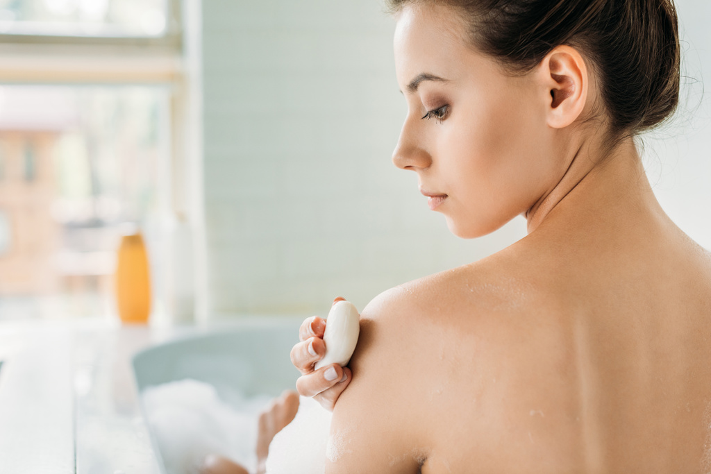 泡付きのバスタブで石鹸で洗う美しい裸の女の子の背面図 - 写真・画像