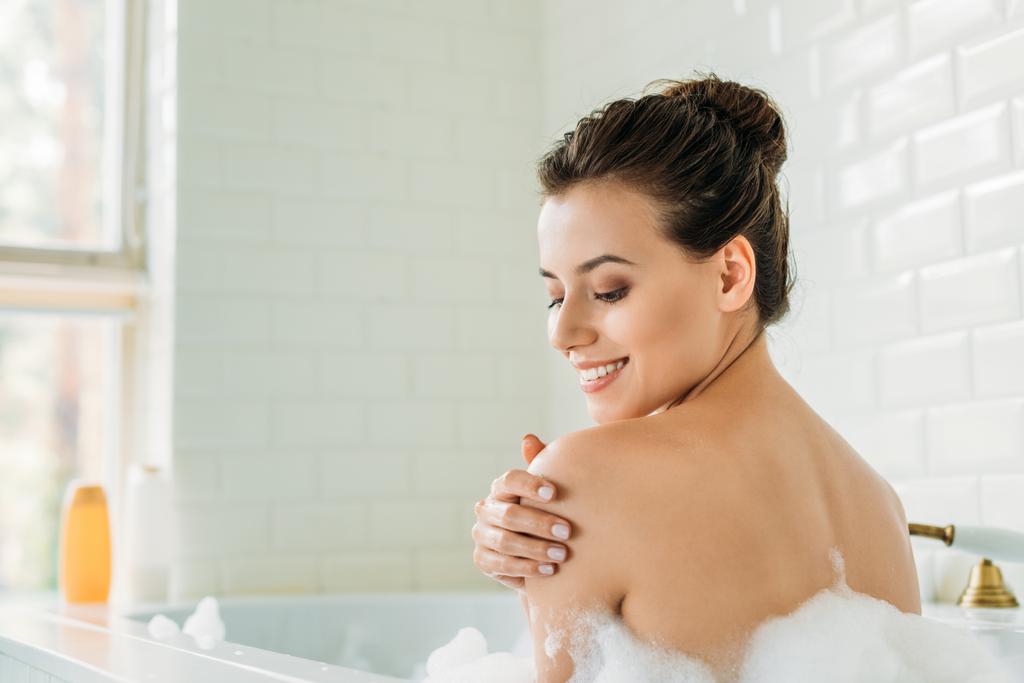 kaunis hymyilevä nuori nainen rentouttava kylpyammeessa vaahdolla
 - Valokuva, kuva