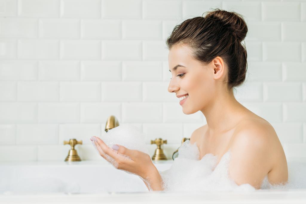 вид сбоку красивой улыбающейся девушки, расслабляющейся в ванне с пеной
 - Фото, изображение