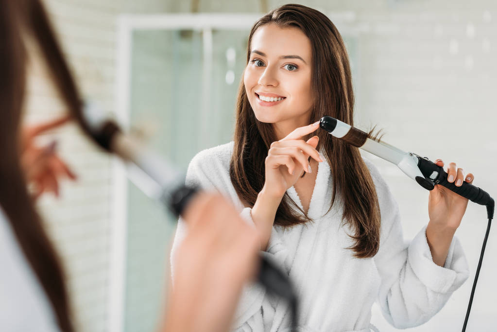Happy tmavovláska v županu pomocí vlasy natáčka na zrcadlo v koupelně  - Fotografie, Obrázek