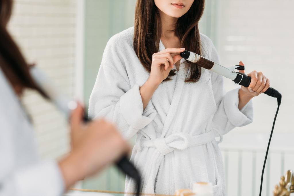 Genç kadının bornoz, banyo aynada Saç Kıvırıcı kullanarak kırpılmış atış   - Fotoğraf, Görsel