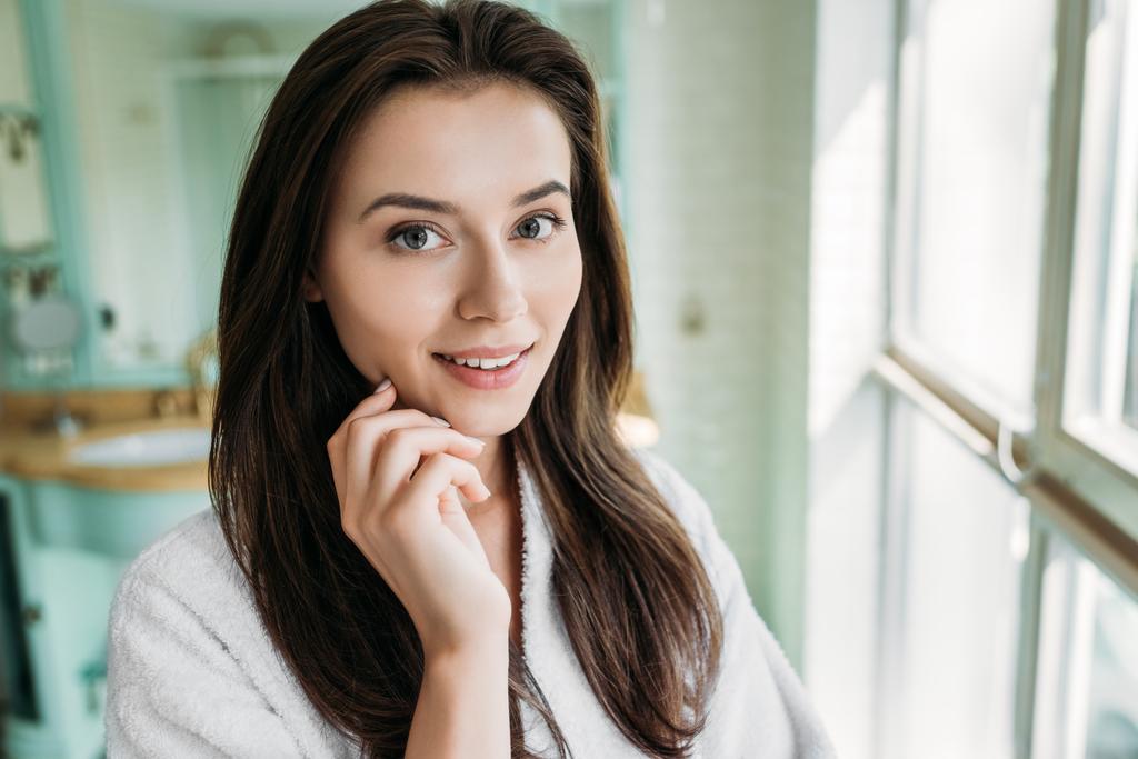 beautiful brunette girl in bathrobe smiling at camera in bathroom - Photo, Image