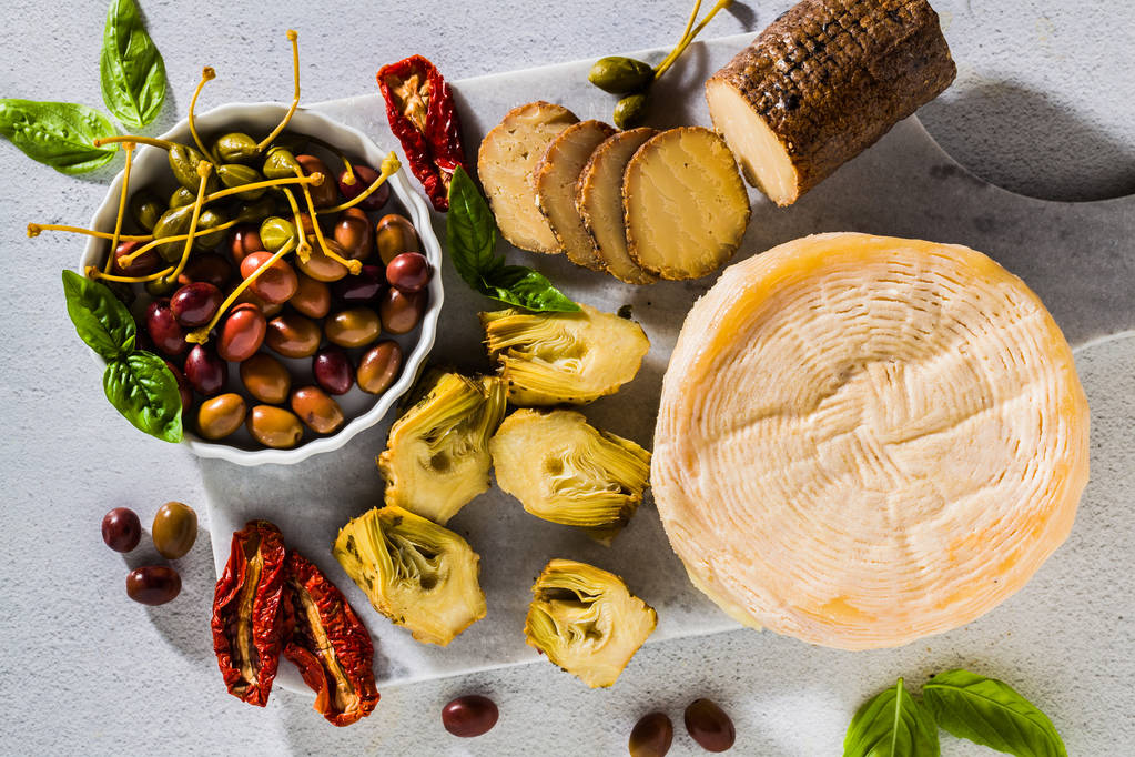 Several types of Italian cheese from Puglia and cold snacks on the table. Artichokes in oil and dried tomatoes - Photo, Image