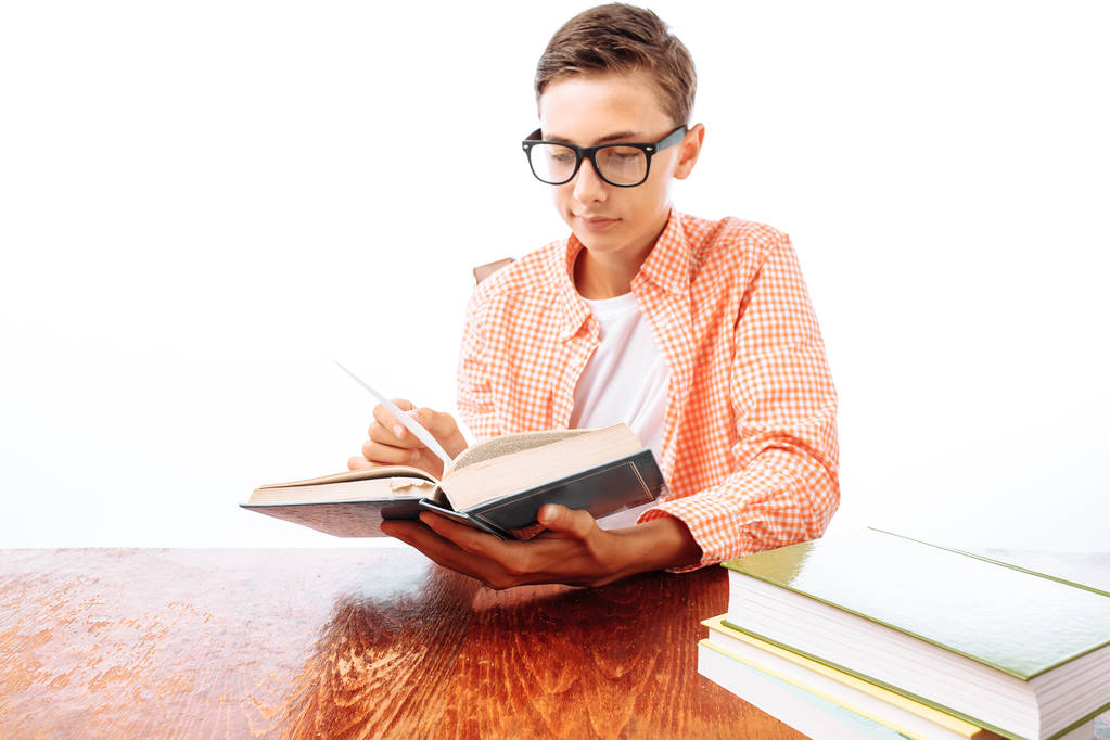 Joven chico adolescente guapo leyendo libro sentado en la mesa, colegial o estudiante haciendo la tarea, en el estudio sobre fondo blanco
 - Foto, imagen