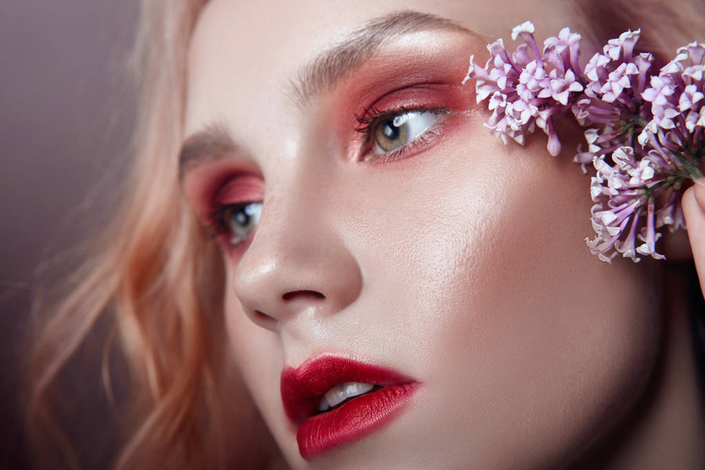 Portrait of a blonde woman with flower petals on her face close-up, bright red makeup and lipstick. Skin hydration, face care, anti-aging effect of cosmetics - Photo, Image