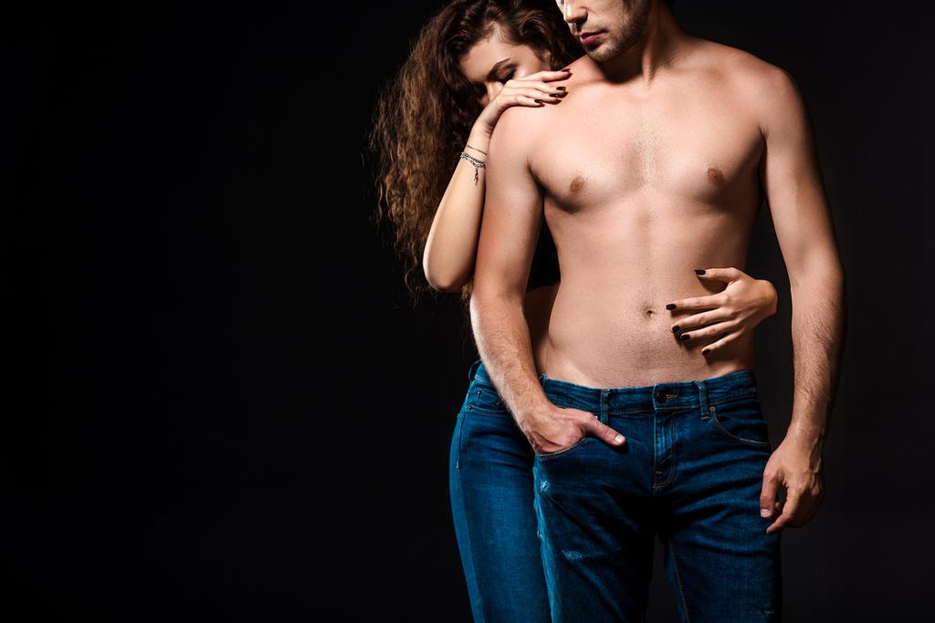 Teilbild der Frau umarmt hemdlosen Freund in Jeans isoliert auf schwarz - Foto, Bild
