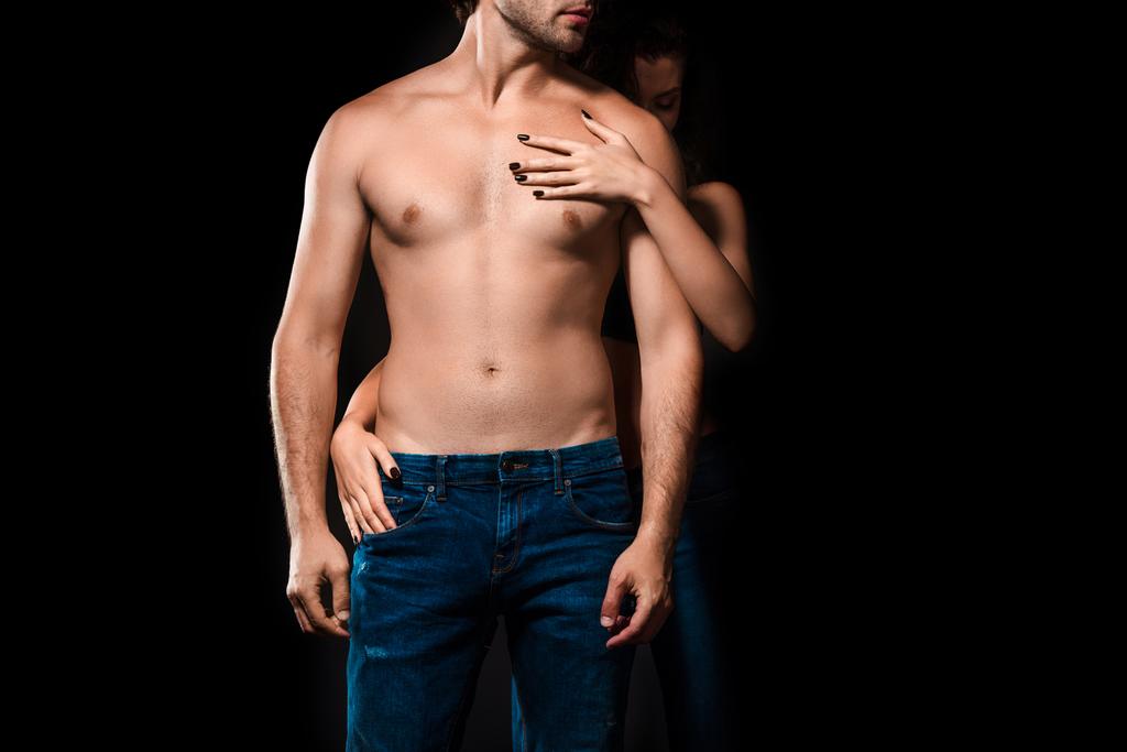 Μερική άποψη της γυναίκα αγκαλιάζει shirtless φίλο σε απομονωμένα σε μαύρο τζιν - Φωτογραφία, εικόνα