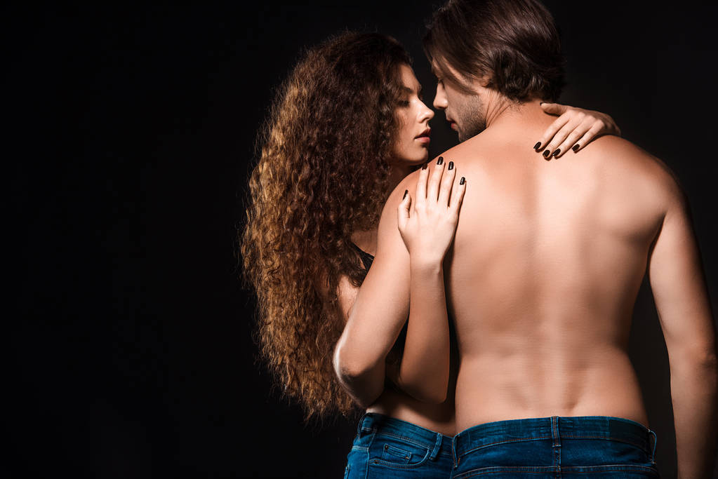 Rückseite der Freundin umarmt hemdlosen Mann isoliert auf schwarz - Foto, Bild