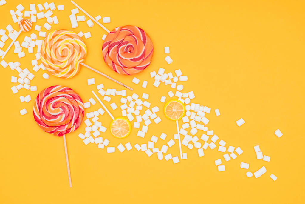 pohled shora rozptýlené marshmallows a lízátka izolovaných na oranžové - Fotografie, Obrázek
