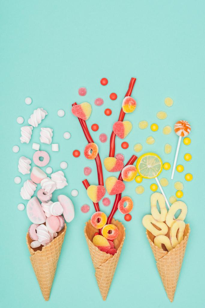 top view of jelly candies, marshmallows, lollipops and waffle cones isolated on turquoise - Photo, Image