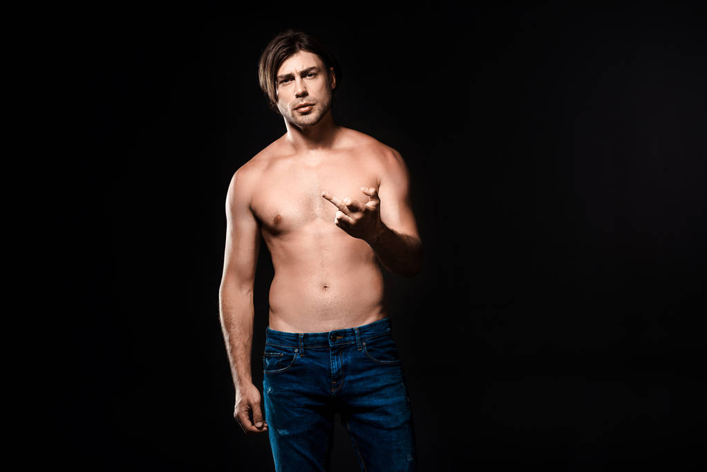 портрет человека без рубашки в джинсах, показывающий средний палец к камере, изолированный на черном
 - Фото, изображение