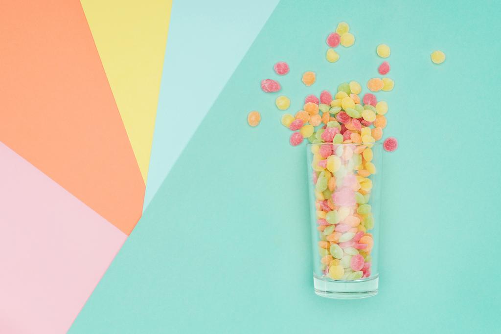 bovenaanzicht van heerlijke verspreide jelly snoepjes en glas op gekleurd oppervlak - Foto, afbeelding