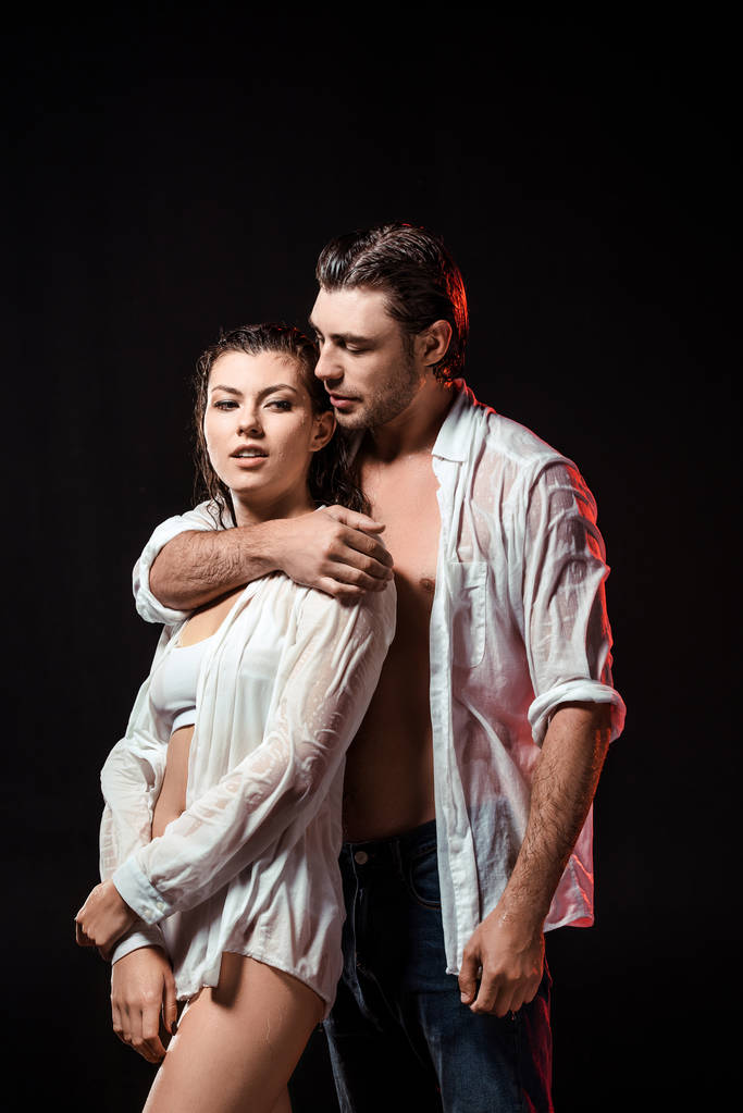 portrait of seductive couple in wet white shirts posing on black backdrop - Photo, Image