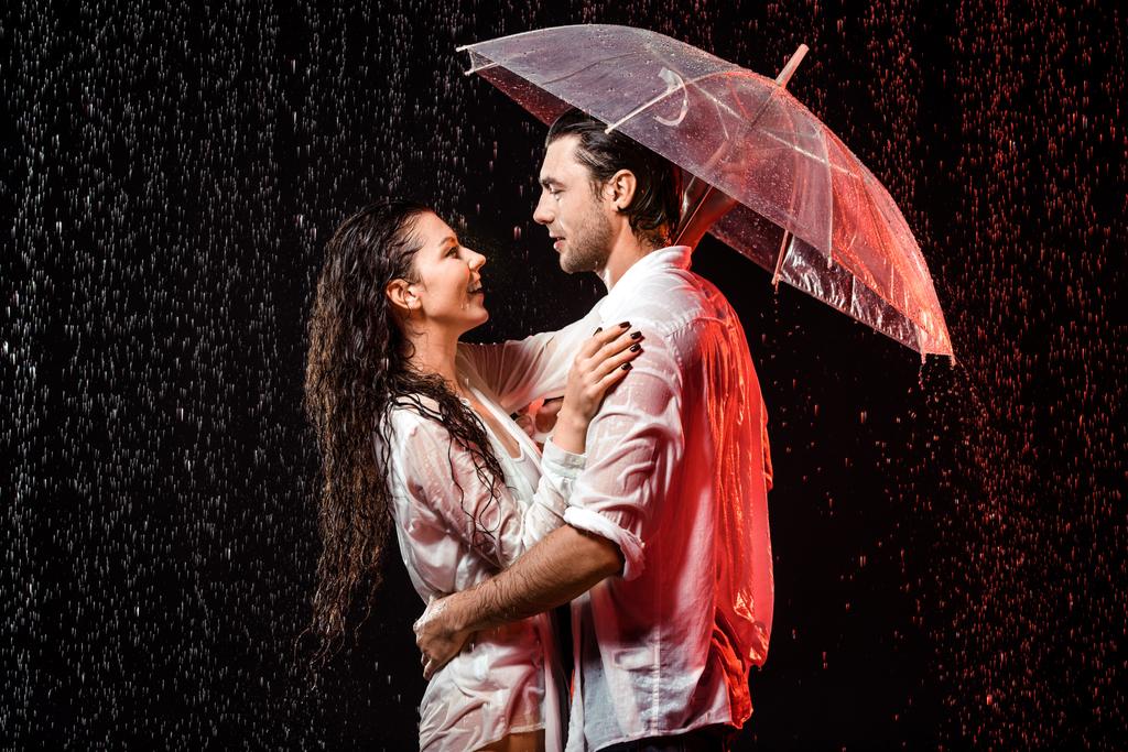 黒の背景に傘雨の下で立ってと白いシャツでロマンチックなカップルの側面図 - 写真・画像