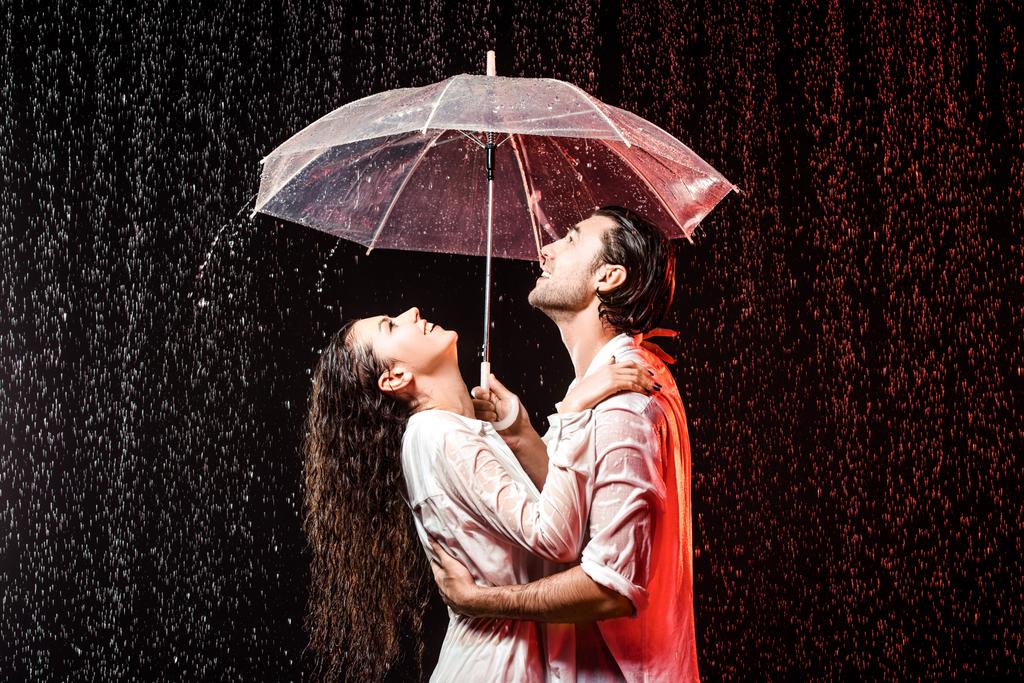 Widok z boku z romantyczna para w białe koszule z parasol stojący pod deszcz na czarnym tle - Zdjęcie, obraz
