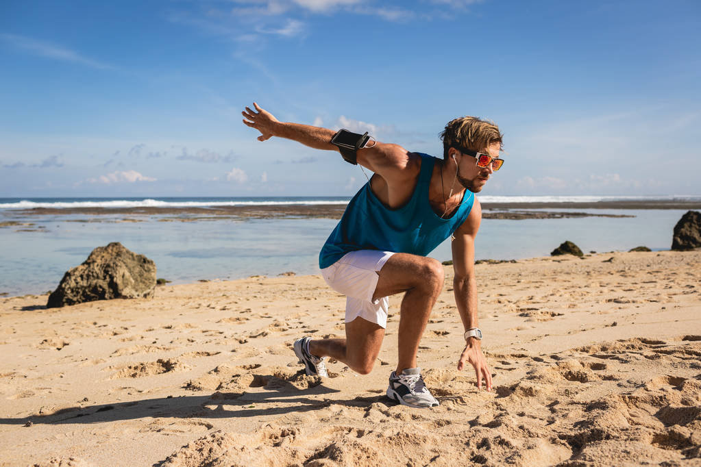 athletic handsome man doing lunges during workout on seashore - Photo, Image