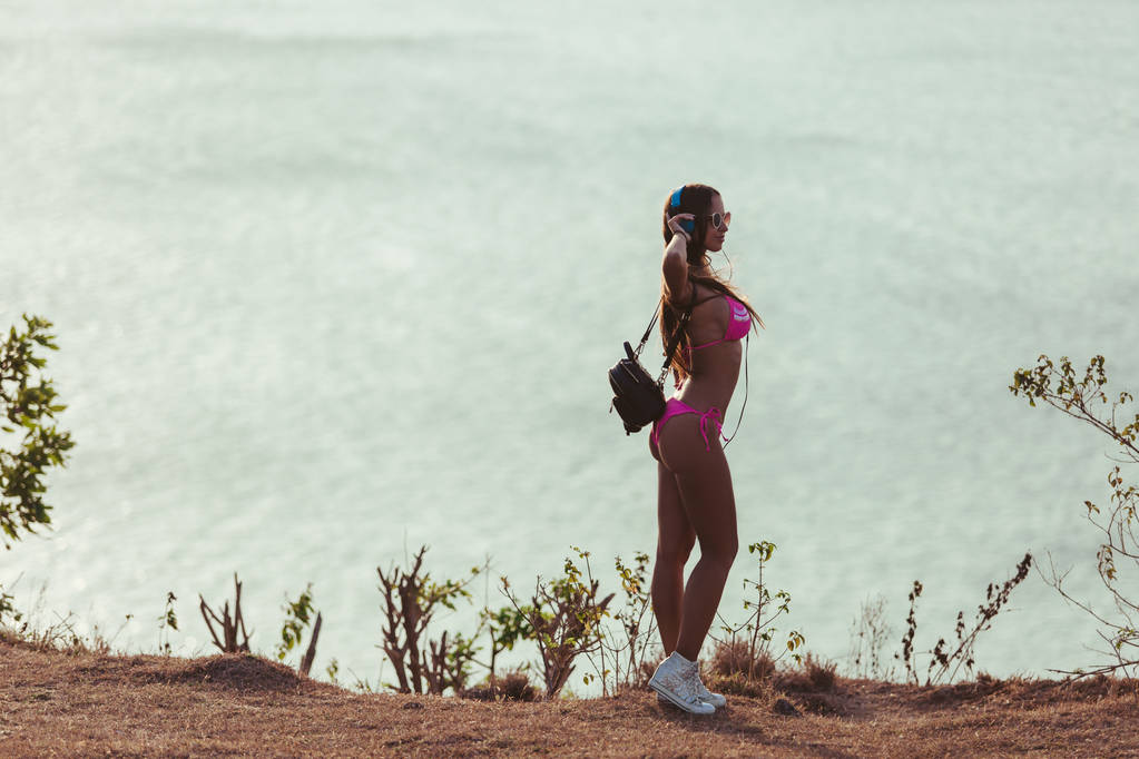 vista laterale di ragazza attraente in cuffia e bikini rosa in piedi sulla costa
 - Foto, immagini