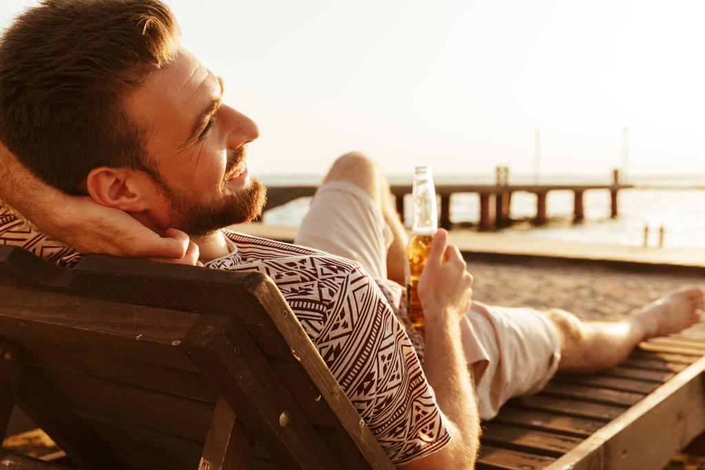 Фото красивого мужчины отдыхающего на пляже, пьющего пиво
. - Фото, изображение