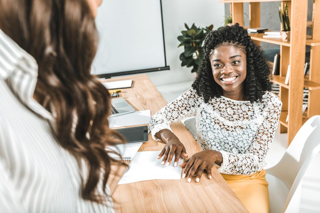 портрет улыбающейся африканской женщины-американки, разговаривающей с коллегой Уайлом, сидящим на рабочем месте в офисе
 - Фото, изображение