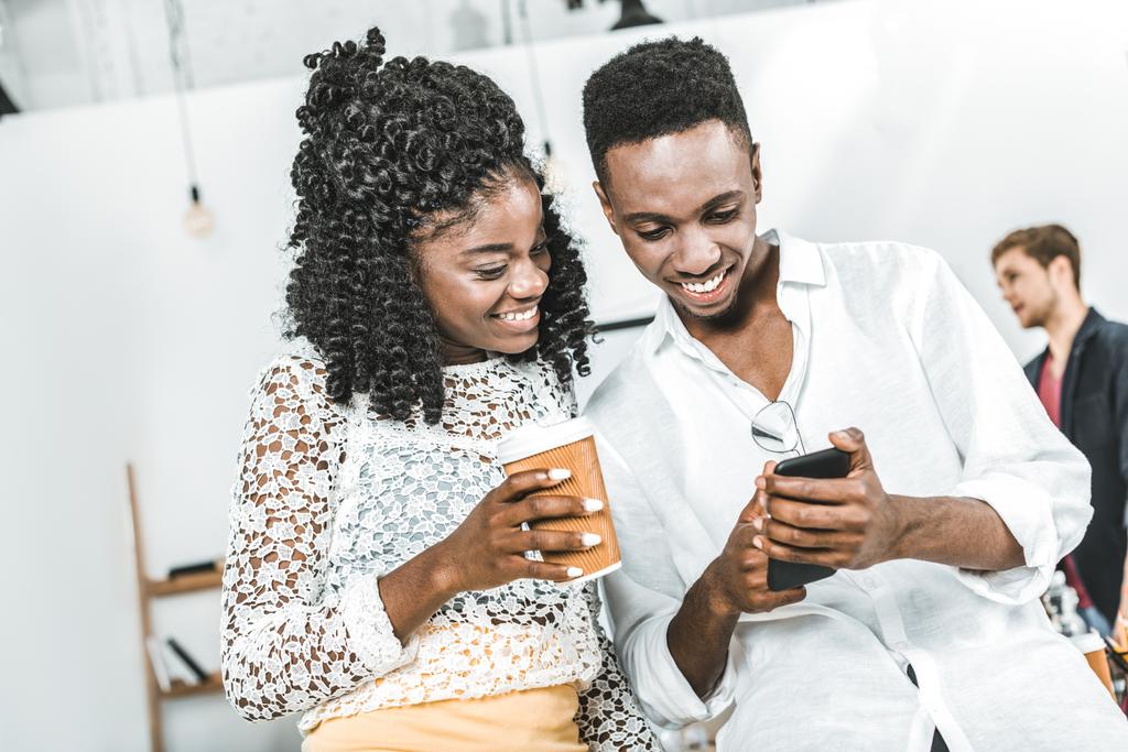 sorrindo afro-americanos empresários usando smartphone juntos no escritório
 - Foto, Imagem