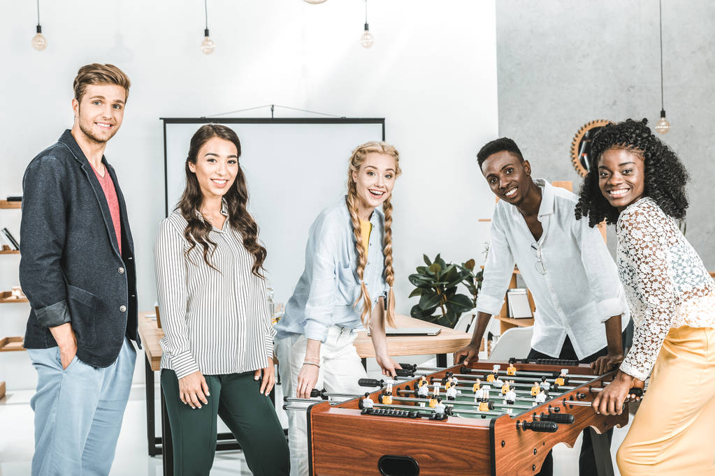 multikulturell lächelnde Geschäftsleute blicken in die Kamera, während sie im Büro Tischkicker spielen - Foto, Bild