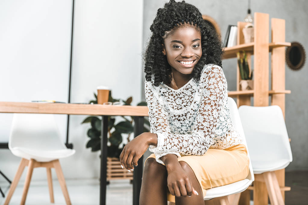 Porträt einer schönen afrikanisch-amerikanischen Geschäftsfrau, die am Arbeitsplatz sitzt und in die Kamera blickt - Foto, Bild